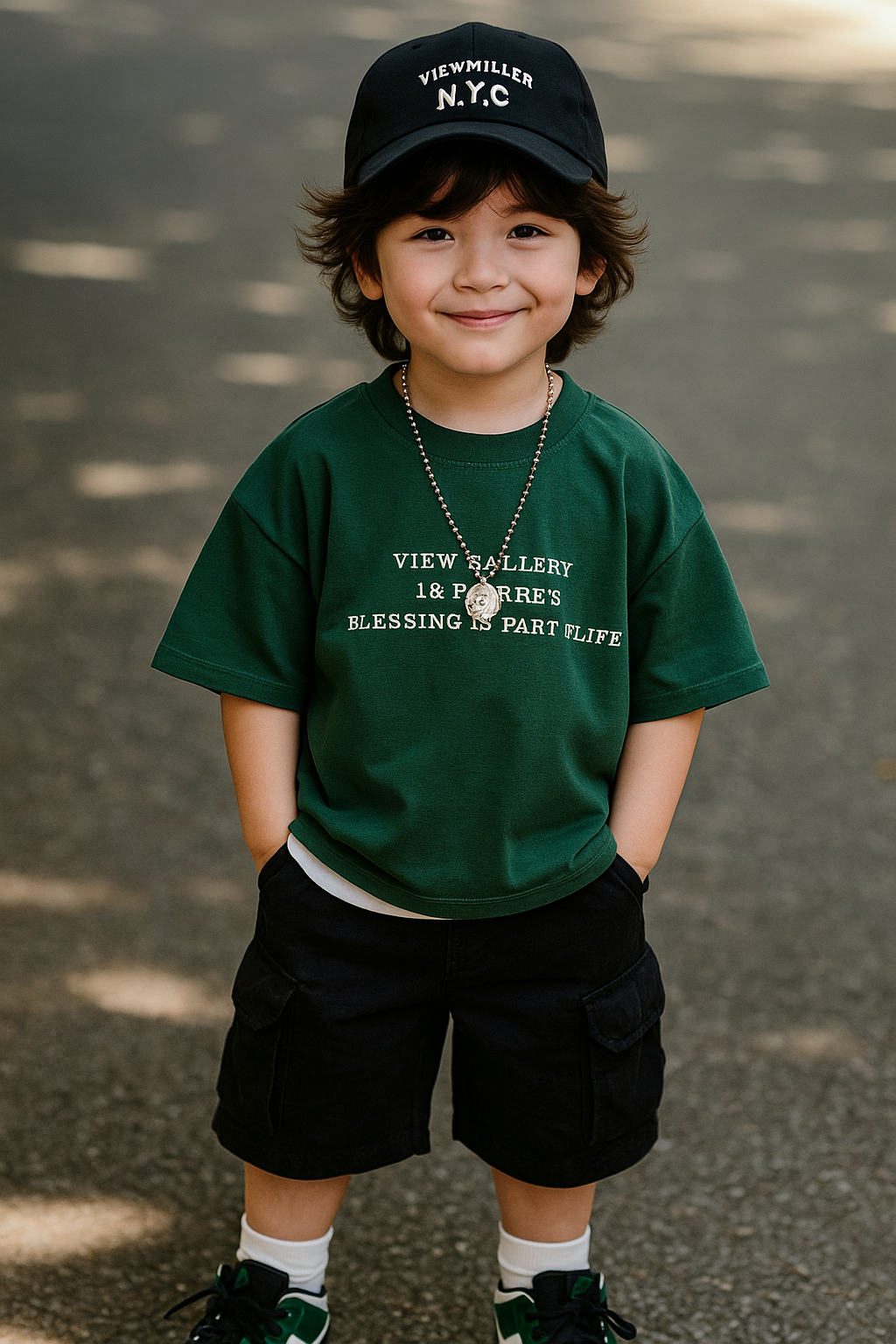 Smiling young boy wearing urban kids clothing including a green graphic t-shirt, black shorts, and a black NYC cap