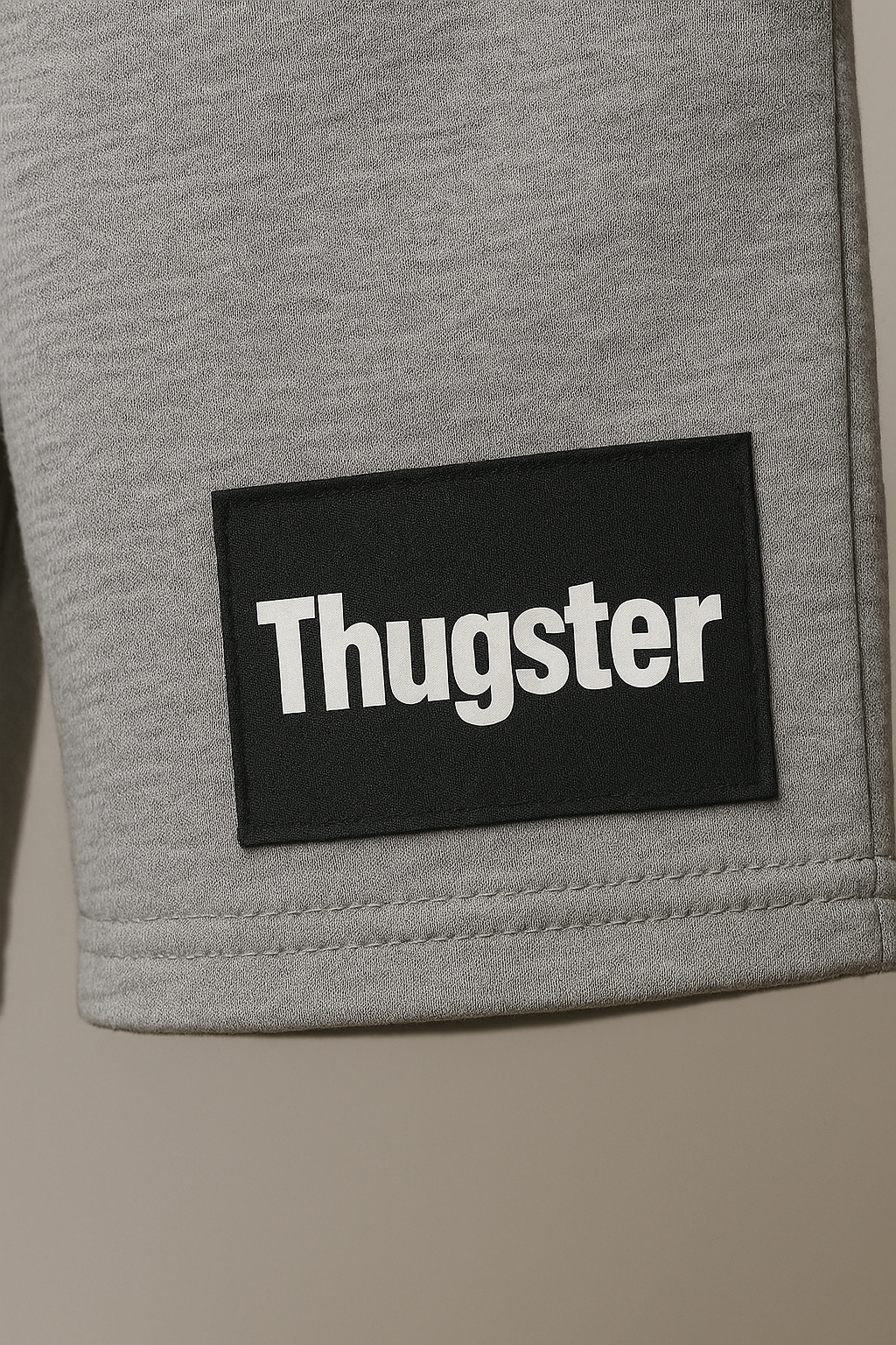 Close-up of grey fabric with black patch labeled Thugster from urban kids clothing set